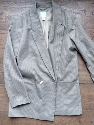 Kavaj - Stilren grå/brun kavaj med rutmönster och oversized passform. Krage, en knapp framtill och två fickor. Perfekt Tunt innerfoder för extra komfort.