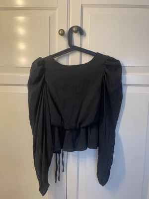 Blus med öppen rygg - Svart blus med puffärmar, öppen i ryggen med tre knyt rosetter 💞 sitter ungefär som xs