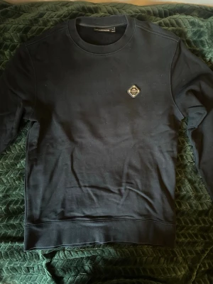 Svart sweatshirt från Lindbergh - En stilren svart sweatshirt från Lindbergh med rund hals och ett diskret märke på bröstet. Tröjan har långa ärmar och är tillverkad i mjukt bomullsmaterial. Perfekt för en avslappnad och trendig look.