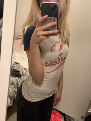 Vit och marinblå t-shirt med tryck - Säljer en vit t-shirt med marinblå ärmar och röd text framtill. T-shirten har kontrastfärgade muddar vid ärmslut och en klassisk rund halsringning. Perfekt för en avslappnad och cool stil.