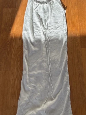 Vit lång stickad klänning med snörning - Lång vit stickad klänning med smala axelband och snygg snörning i midjan och ryggen. Klänningen har en figurnära passform och öppen rygg, vilket ger en trendig och somrig look. Perfekt för varma dagar och strandhäng.