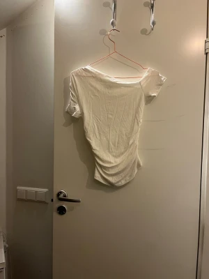 Vit offshoulder topp med rynk -  vit offshoulder topp med korta ärmar och snygg rynkdetalj på sidan. Har aldrig använt tröjan för att det är för liten, tröjan har inga hål eller skador.