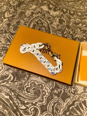 Louis Vuitton vitt kedjearmband - Säljer ett vitt kedjearmband k*pia LV med blå och ljusblå detaljer samt LV-loggor på länkarna. Box medföljer.