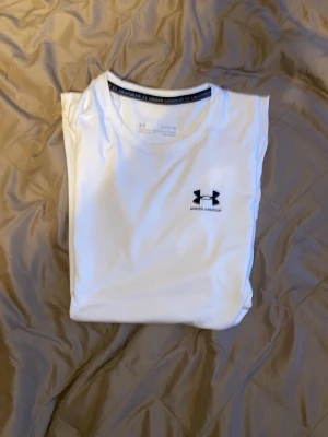 Vit Compression shirt från Under Armour - Snygg vit träningströja från Under Armour med rund hals och korta ärmar. Tillverkad i ett lätt och snabbtorkande funktionsmaterial som passar perfekt till gymmet eller löprundan. Diskret logga i svart på bröstet för en clean sportig look.