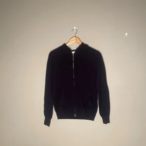 Kashmir/Cashmere Zip-Hoodie från Sayless - Mörkblå Kashmir zip-up hoodie från Sayless med dragkedja framtill och två fickor. Klassisk passform med ribbade muddar vid ärmar och nederkant. Perfekt för en avslappnad stil och lätt att matcha med andra plagg. Huva med dragsko för extra komfort.