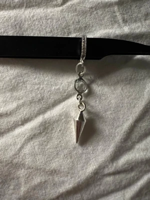 Silvrigt örhänge med konformad detalj - Unikt örhänge i silverfärg med en konformad hängande detalj och en rund, transparent pärlliknande dekoration ovanför. Snygg och edgy design som sticker ut och passar dig som gillar statement-accessoarer. 69kr/st 110kr/par