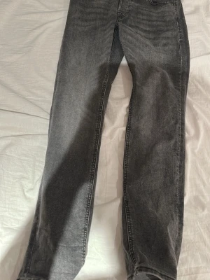 Jack and Jones jeans - Snygga grå jeans fårn Jack and jonea med raka ben och klassisk femficksmodell. Jeansen har en svart patch bak i midjan och tydliga sömmar. Perfekta för en avslappnad och trendig look.