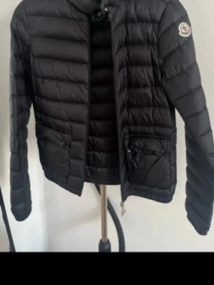 Svart dunjacka från Moncler Lans xxs svart  - Snygg svart dunjacka från Moncler med quiltad design och rund hals. Jackan har två framfickor med lock och dragkedja samt Moncler-logga på ärmen. Kvitto finns självklart 