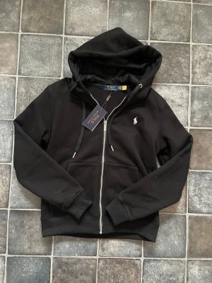 Svart Polo Ralph Lauren Hoodie - Tja, säljer denna Hoodien från Ralph lauren då den var för liten för mig. Aldrig använd, skick 10/10. Nypris ca 1900kr. Riktigt skön rekommenderar starkt. Hör av er vid funderingar!