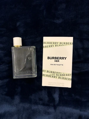 Burberry Her Eau de Toilette 100 ml - Burberry Her Eau de Toilette är en fräsch parfym i en stilren, transparent glasflaska med vit kork och klassisk Burberry-logga. Flaskan rymmer 100 ml och kommer i en vit kartong med gröna Burberry-detaljer. Perfekt för dig som gillar eleganta och moderna dofter. Luftar lite sött men fortfarande fräscht och gott. Originalpris var ungefär 1200. Meddela om frågor om priset eller vad som helst