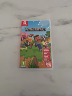 Minecraft till Nintendo Switch - Minecraft till Nintendo Switch, komplett med fodral och spelkassett. Omslaget har färgglad grafik med karaktärer och blockig värld i grönt, blått och brunt. Perfekt för dig som gillar kreativt byggande och äventyr.