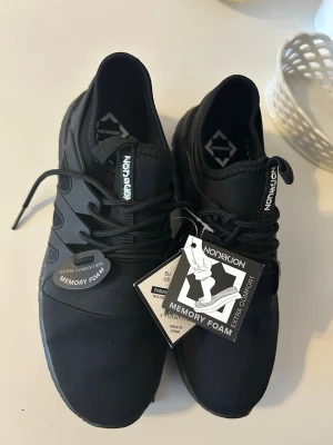 Svarta sneakers från Nordlion - Svarta sneakers från Nordlion med modern design och memory foam-sula för extra komfort. Skorna har snörning, diskret logga på plösen och ovandel i textil och syntet. Snygga detaljer på sidorna och robust, mönstrad yttersula.