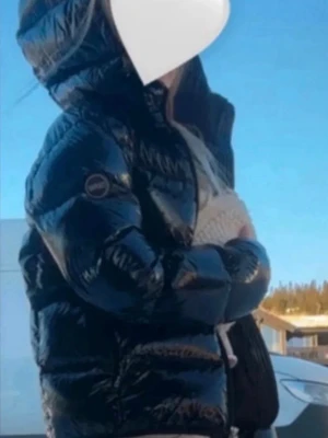 Svart glansig pufferjacka Colmar - Säljer en svart, glansig pufferjacka från Colmar med huva och dragkedja framtill. Perfekt för kalla dagar och riktigt snygg till streetwear-stilen. Den är alldrig använd av mig pga att den är för kort i armarna för mig, jag är 171 cm. Köpte den av en annan tjej som knappt använt den heller.💕Jättebra skick.