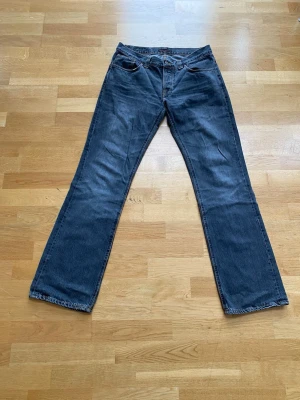 Mörkgrå bootcut ola nudie jeans vintage  - Säljer ett par mörkgrå bootcut Ola jeans från Nudie Jeans med klassisk femficksmodell och kontrastsömmar. Hör av dig vid minsta lilla fråga. Skick 7,5/10 W34 L34