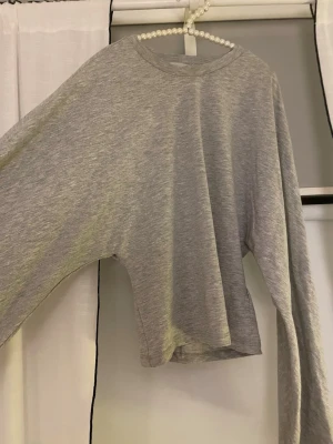 Grå figursydd långärmad tröja - Enkel och stilren grå långärmad tröja i figursydd modell med vida ärmar och rund halsringning. Tillverkad i mjukt och tunt material som känns skönt mot huden. Perfekt för en avslappnad och trendig look.