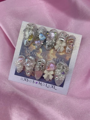 BunnyBella (M);Medium Almond - Säljer ett set handgjorda press-on naglar i silver och rosa toner med holografiskt glitter. Naglarna har en medium mandel form och är dekorerade med 3D-bows, pärlor, hjärtan och metalliska detaljer för en extra lyxig look. Perfekt för dig som vill sticka ut!M: 16 mm, 12 mm, 12,5 mm, 11,5 mm, 10 mm