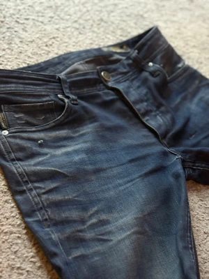 Vintage jeans - Säljer ett par mörkblå jeans  med slitningar och distressed detaljer på benen. Jeansen har klassisk femficksmodell, knappgylf och smal passform. Materialet är denim med stretch för extra komfort. Perfekta för en avslappnad och trendig look.