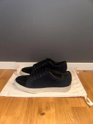 Lanvin skor - Snygga mörkblå sneakers med svart tåparti och vit sula. Skorna har ovandel i mocka och detaljer i läder, samt svarta skosnören och metallöljetter. Perfekta för dig som gillar stilrena och klassiska sneakers med en twist. Size 43/UK8, dustbag ingår.