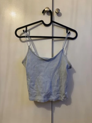 Ljusblå ribbad linnetopp - Säljer en ljusblå ribbad linnetopp med tunna axelband. Toppen har en croppad passform och är perfekt för varma dagar. Enkel och stilren design som passar till mycket. Perfekt att matcha med jeans eller kjol.