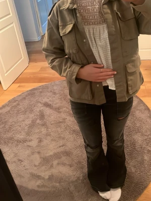 Beige overshirt med fickor - Stilren beige overshirt med stora fickor framtill och klassisk krage. Jackan har en rak passform och knäpps med knappar. Perfekt att slänga över en tröja för en avslappnad look.