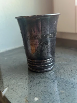 Silverbägare Jämtlandsk-serien 1950 - Unik silverbägare från Jämtlandsk-serien, tillverkad av GAB och daterad 1950. Bägaren har en klassisk form med ingraverad text och stämplar i botten. Perfekt för samlare av antikt silver eller som dekorativ detalj. Äkta silver 830 39gm