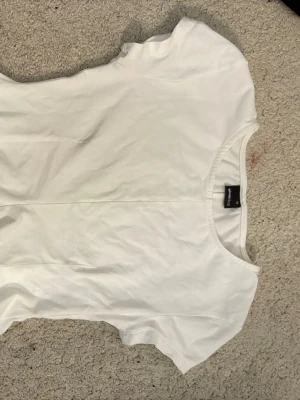 Vit t-shirt med utsvängda volanger från Gina tricot  - En enkel vit t-shirt från Gina  med rund halsringning och korta ärmar. Tillverkad i mjuk bomull som känns skön mot huden. Perfekt att matcha med jeans eller shorts för en clean look. Flängfri och använda fåtalgånger pågrund av att den är fel storlek för mig. 