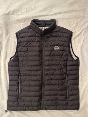Svart dunväst från Colmar - Snygg svart dunväst från Colmar med quiltad design och hög krage. Västen har två dragkedjeförsedda fickor och ett Colmar-märke på bröstet. Perfekt för lager-på-lager och håller dig varm under kyliga dagar.
