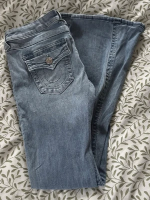 Ljusblå bootcut jeans True Religion - Säljer ett par ljusblå bootcut jeans från True Religion, perfekt nu till våren! Byxorna är uppsydda och är ungefär 81cm i Innebenslängd 