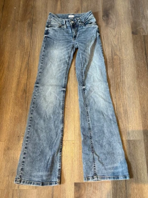 Blå bootcut jeans med detaljer - Ett par blå bootcut jeans med fina detaljer och klassisk femficksdesign. Jeansen har knapp- och dragkedjegylf samt dekorativa ficklock med knappar bak. Tillverkade i denim med en tvättad look.