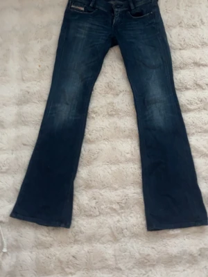 Mörkblå bootcut jeans - Säljer ett par mörkblå bootcut jeans med lätt slitning framtill och klassiska fem fickor. Jeansen har en snygg tvätt och utsvängda ben, perfekta för en avslappnad och trendig look.
