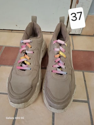 Beige chunky sneakers med färgglada snören - Chunky sneakers i beige med tjock sula och färgglada skosnören i rosa, gult och blått. Skorna har en sportig look och är tillverkade i syntetmaterial med meshdetaljer för extra komfort. Perfekta för dig som gillar streetstyle och vill sticka ut.