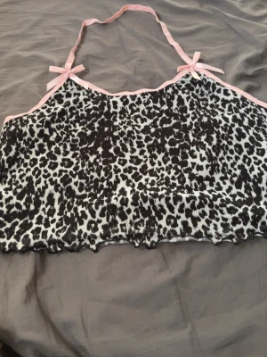 Leopardmönstrad mesh body med rosetter - Säljer en leopardmönstrad mesh body med tunna rosa axelband och söta små rosetter vid axlarna. Materialet är genomskinligt mesh och har vågig kant nedtill. Perfekt för dig som gillar djurmönster och detaljer i pastell.