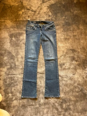 Blå bootcut jeans från pepe jeans - Säljer ett par klassiska blå bootcut jeans från Pepe jeans med låg midja. Jeansen har fem fickor, dragkedja och knapp framtill samt snygga slitningar för en avslappnad look. Perfekta till sneakers eller boots. Lång på mig som är 167