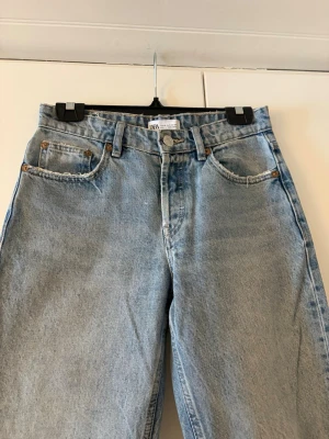 Ljusblå raka jeans från Zara - Säljer ett par ljusblå raka jeans från Zara med låg midja enligt mig. Jeansen har slitna detaljer på bakfickorna. Perfekta till sneakers eller boots!