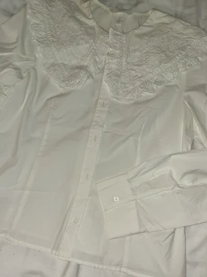 Vit skjorta med broderad krage - Stilren vit skjorta med stor dekorativ broderad krage och knappar framtill.