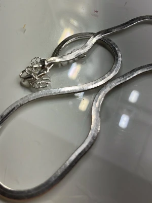 Silvrigt ormkedjehalsband - Säljer ett stilrent halsband i ormkedjemodell med slät, glänsande yta. Halsbandet är i silverfärgat metallmaterial och har ett klassiskt lås. Perfekt för dig som gillar minimalistiska accessoarer med modern känsla.