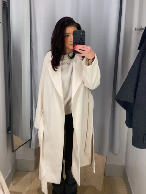 Ljusbeige lång kappa med slits - Stilren ljusbeige kappa med lång, rak passform och breda slag. Kappan har öppen front och slits i sidorna för extra rörelsefrihet. Perfekt för dig som gillar minimalistisk och trendig stil. Passar till både jeans och klänning.