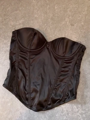 Tubtopp korsett  - Korsett aktig tub topp i svart från H&M. Går att spänna i tre olika storlekar i ryggen med metallspännen