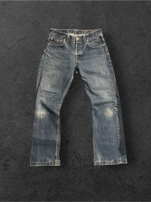 Levi's 555 blå raka jeans | W32 L32 - Klassiska blå Levi's 555 jeans med raka ben och knappgylf. Jeansen har en vintage tvätt med slitningar vid knäna och bakficka med den ikoniska röda Levi's-lappen. Tillverkade i kraftig bomullsdenim för en tidlös look.