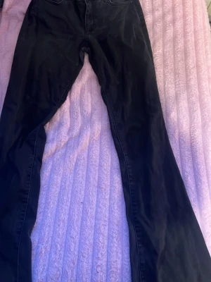 Svarta bootcut jeans - Säljer ett par svarta bootcut jeans med klassisk femficksdesign. Jeansen har utsvängda ben och normal midja, perfekta för en trendig och avslappnad look. Materialet känns mjukt och följsamt, vilket gör dem sköna att bära hela dagen.