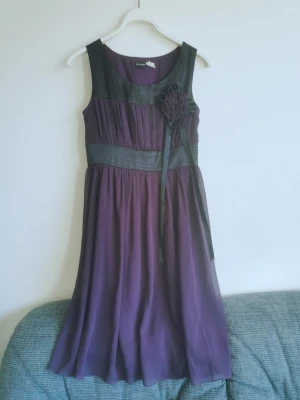 Bodyflirt lila klänning med blomdetalj - Lila och svart fodrad knälång klänning med löstagbar blomdetalj. Står som 36 men funkar för mig som har 36/38. 