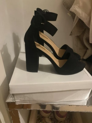 Svarta chunky pumps med ankelrem - Säljer ett par svarta pumps från VICENZA med bred klack och öppen tå. Skorna har en snygg ankelrem med spänne och är gjorda i mockaimitation. Perfekta för dig som gillar chunky klackar och stilren design.