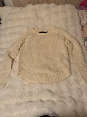 Krämvit stickad tröja Vero Moda - Säljer en krämvit stickad tröja från Vero Moda. Tröjan har ett snyggt strukturmönster, rund halsringning och ribbade muddar vid ärmslut och nederkant. Perfekt för lager på lager och riktigt mysig till hösten och vintern men också på vår och sommar. 