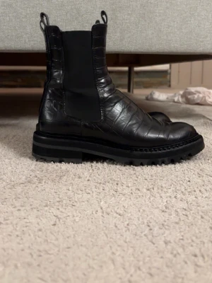Svarta Billi Bi boots i croco  - Hej! 👋 Säljer ett par svarta skinnboots från Billi Bi med crocopräglad yta och kraftig sula. Skorna är gjorda i blankt skinn och har elastiska sidopaneler som gör dem enkla att ta på och av. Perfekta för en stilren men bekväm look.  Använda vid få tillfällen. Visst slitage finns på insidan (se bild), men inget som märks vid användning. Nypris: 2499 kr🫶