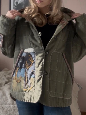 Grön quiltad jacka med elefantmotiv - En handsydd grön typ ”quiltjacka” med elefantmotiv på. Passar jättebra nu som en cool vårjacka! Jag på bilden brukar bära storlek XS som referens   Mått:   Axel: 45cm Bröst: 59cm Längd: 68cm Armlängd: 62cm