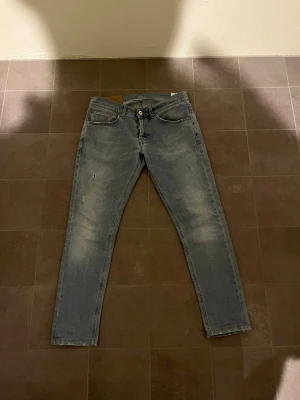 Dondup George W32 - Ett par ljusblåa skinny fit jeans med rak passform och slitningar på vänster lår. Jeansen har subtila slitdetaljer för en avslappnad look. Materialet är denim i bomull. Perfekta för en casual stil. Hör av dig vid minsta lilla fundering, eller prisförslag