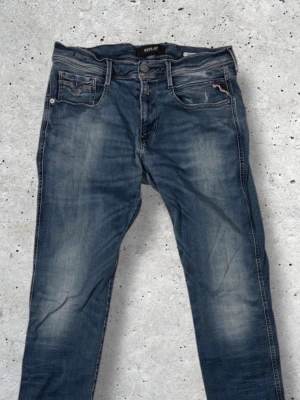 Blå Replay jeans med slitningar - Säljer ett par blå jeans från Replay med snygga slitningar och tvättade detaljer. Klassisk femficksmodell med raka ben och låg midja. Jeansen har Replay-logga på bakfickan och är gjorda i mjuk bomullsdenim.