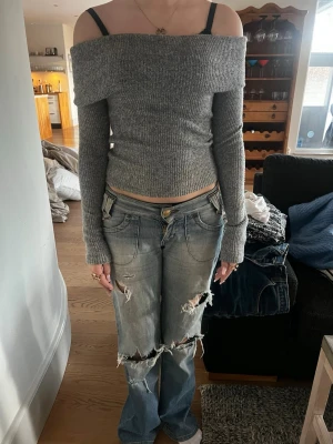 Ljusblå slitna jeans med bootcut - Säljer ett par ljusblå jeans med slitna detaljer och bootcut-modell. Jeansen har låg midja, klassiska fickor och knappgylf. Perfekt för dig som gillar en edgy och avslappnad stil.