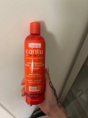Cantu Curl Activator Cream 355 ml - Fuktgivande curl activator cream från Cantu med sheasmör. Passar naturliga lockar, coils och vågor. Ger glans, definierar lockar och gör håret mjukt. Kommer i en orange plastflaska med lock. Innehåller 355 ml.