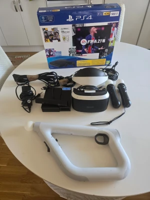 PlayStation 4 med VR och tillbehör - PlayStation 4-konsol med 500GB hårddisk, VR-headset, två Move-kontroller, Aim Controller och kablar. Konsolen är svart och VR-headsetet är svart och vitt. Perfekt för gaming och VR-upplevelser. Originalkartong medföljer.
